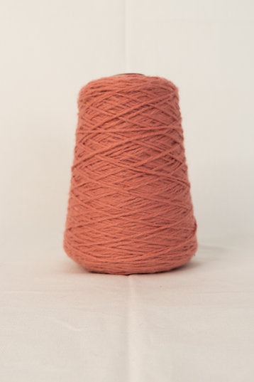 A cone of tufting yarn in a coral color, placed on a neutral background.
