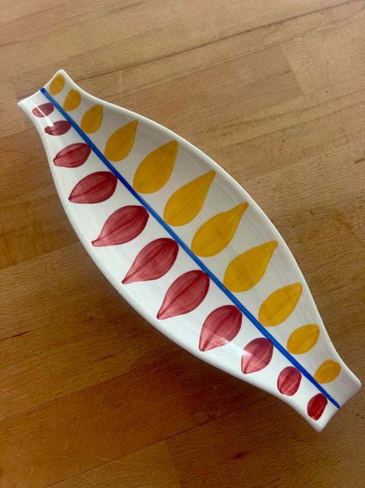 Decorative ceramic dish with red and yellow leaf patterns on a wooden workbench