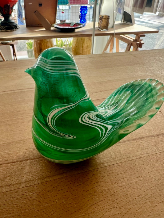 Green and white glass bird figurine on a wooden workbench