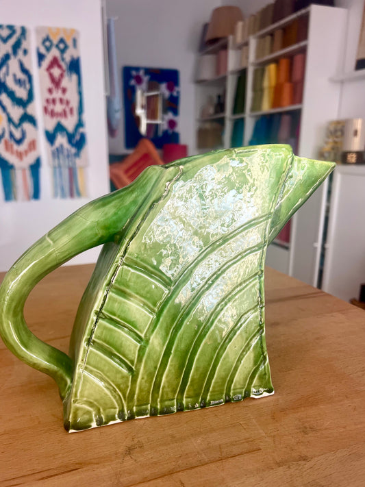 Green ceramic pitcher on a wooden surface with a blurred background