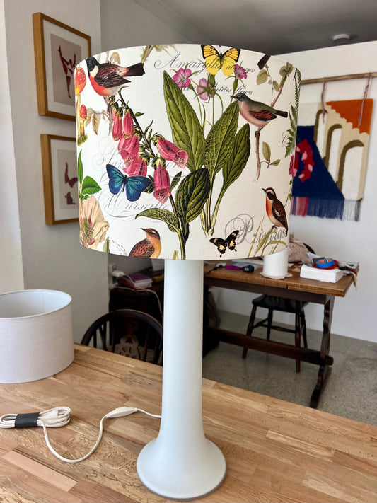 Luxus white glass lamp base with a decorative lampshade featuring floral and bird patterns sits on a wooden table.