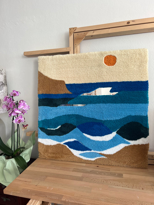A framed tufted wall hanging featuring a vibrant beach scene with blue and green waves, a sun, and a mirrored accent.