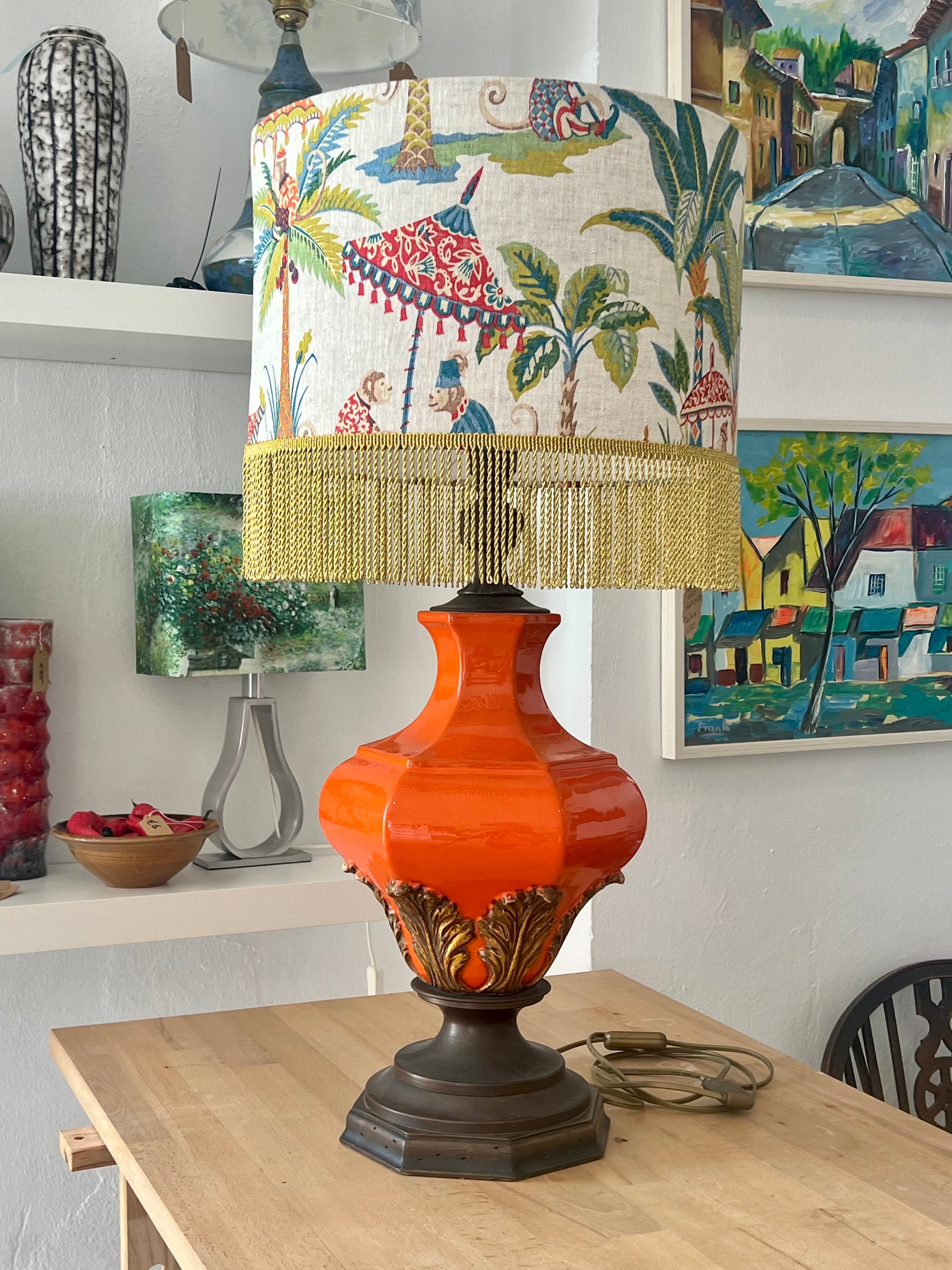 Large orange ceramic decorative table lamp with a colorful linen lampshade on a wooden workbench