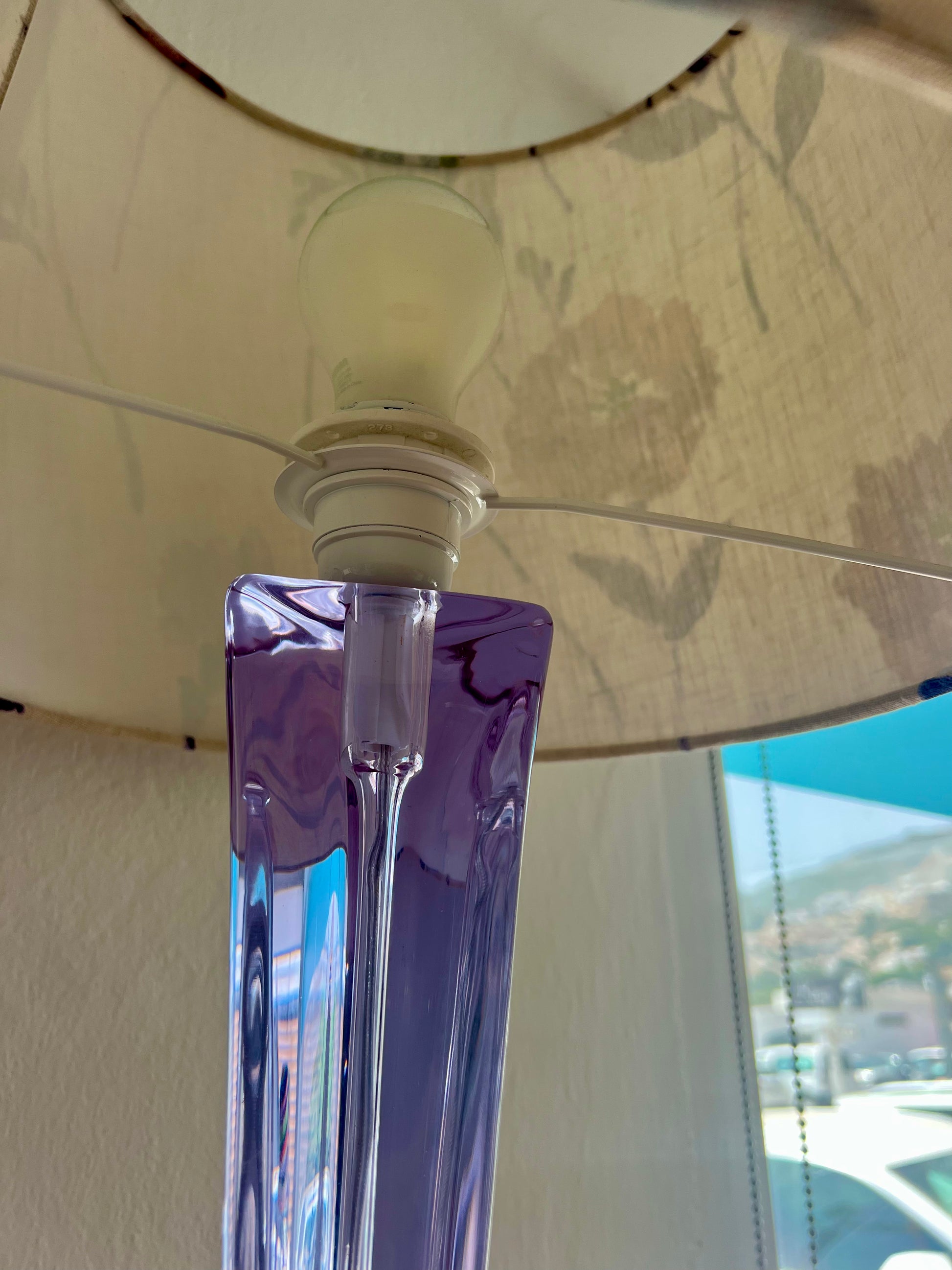 Close-up of a glass lamp with a purple base and beige lampshade with white interior