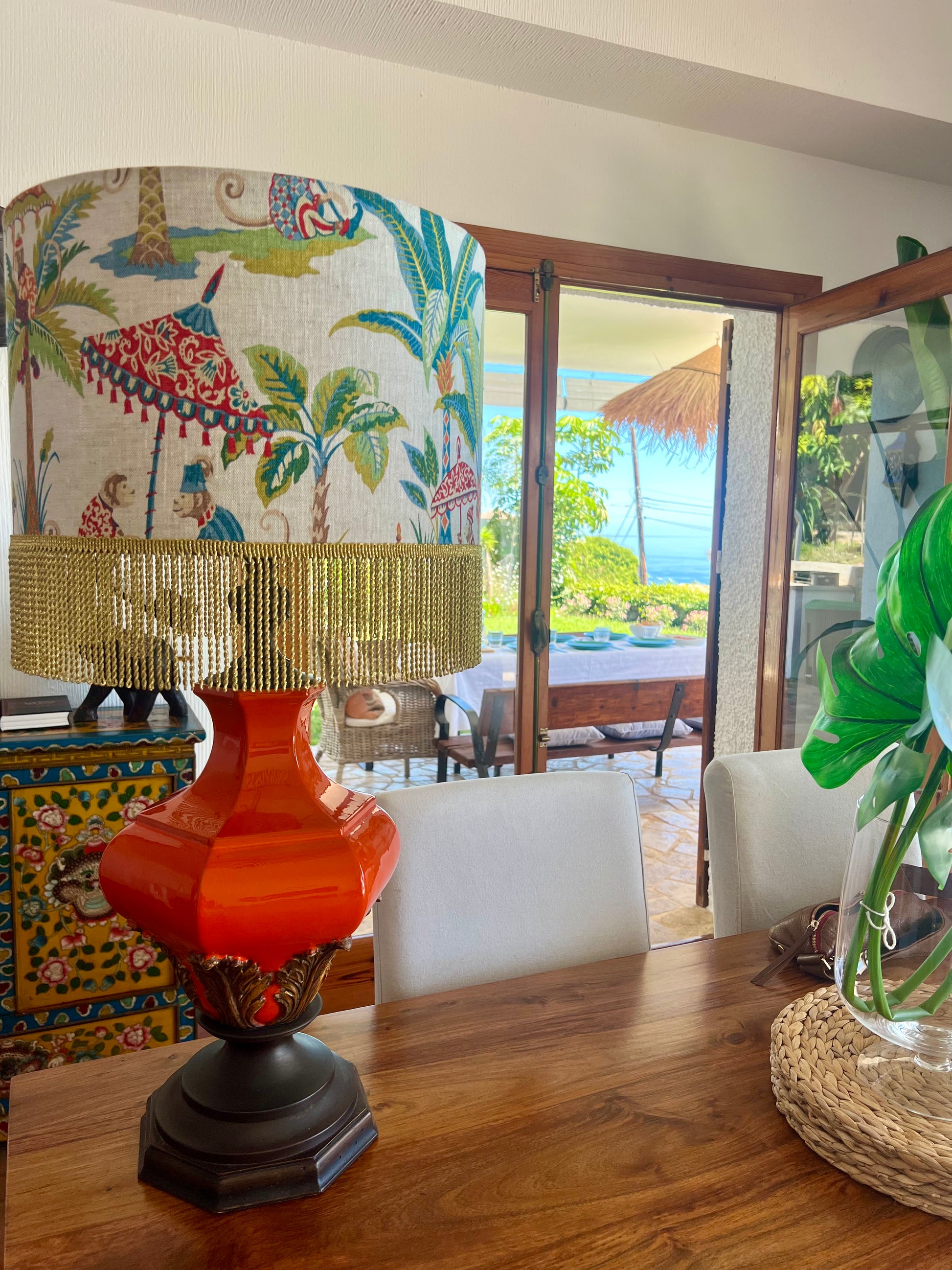 Decorative orange ceramic lamp with a colourful lampshade with monkeys and parasols with gold fringe