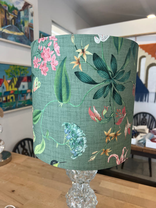 Floral-patterned green lampshade on a crystal lamp base with a room background