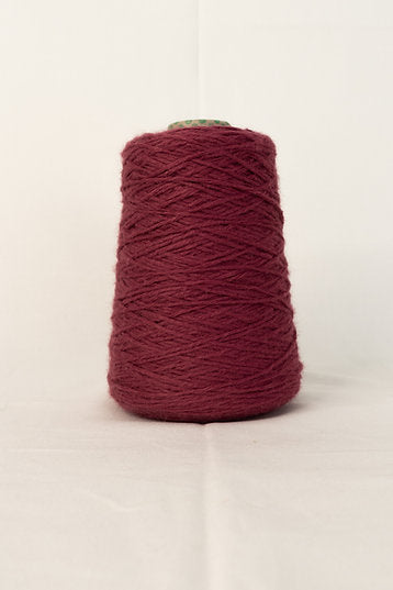 A cone of mauve-colored acrylic yarn placed against a neutral background.