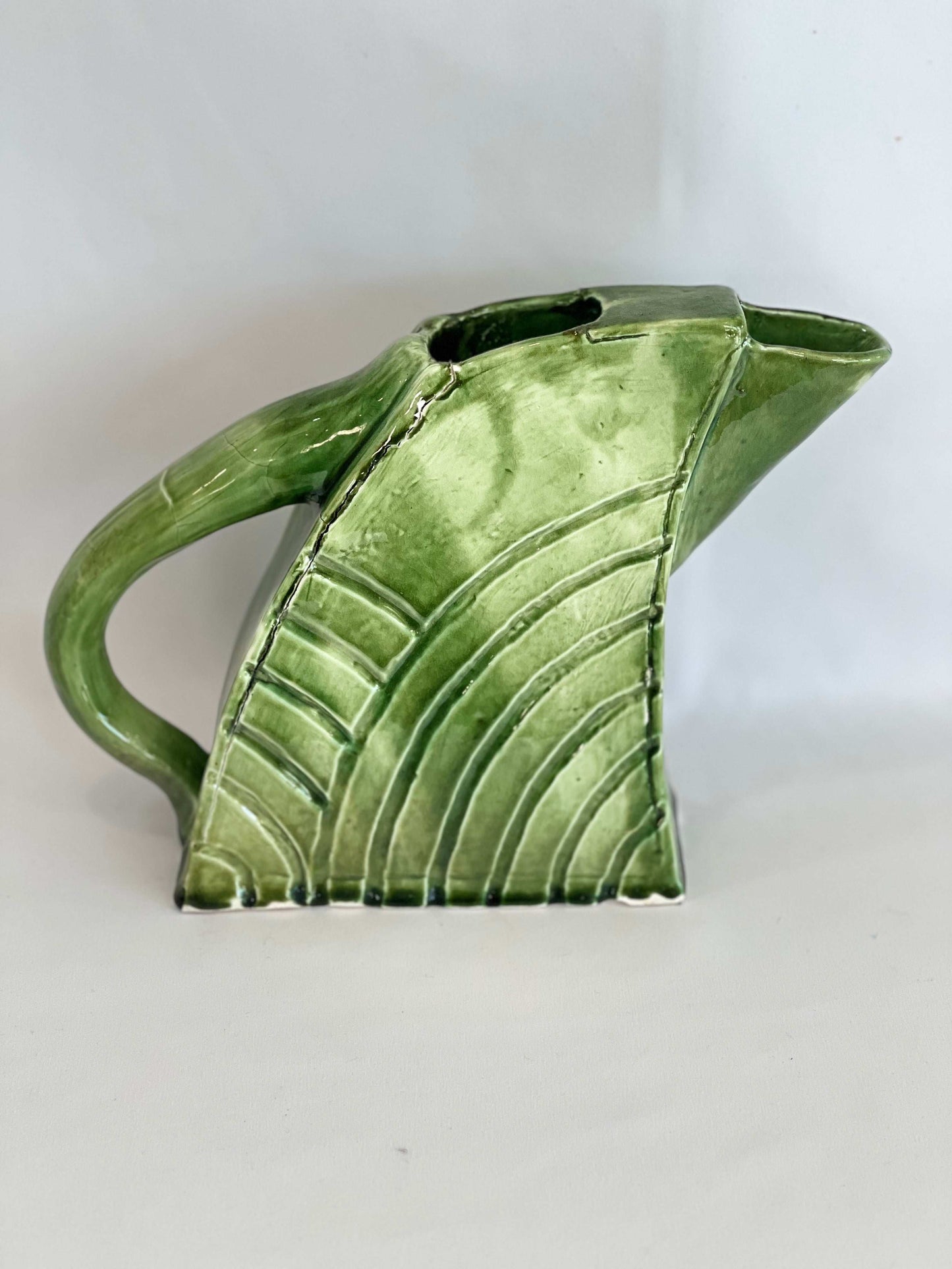 A mossy green ceramic jug with a handle and spout, showing slight cracking which adds to its handcrafted appearance.
