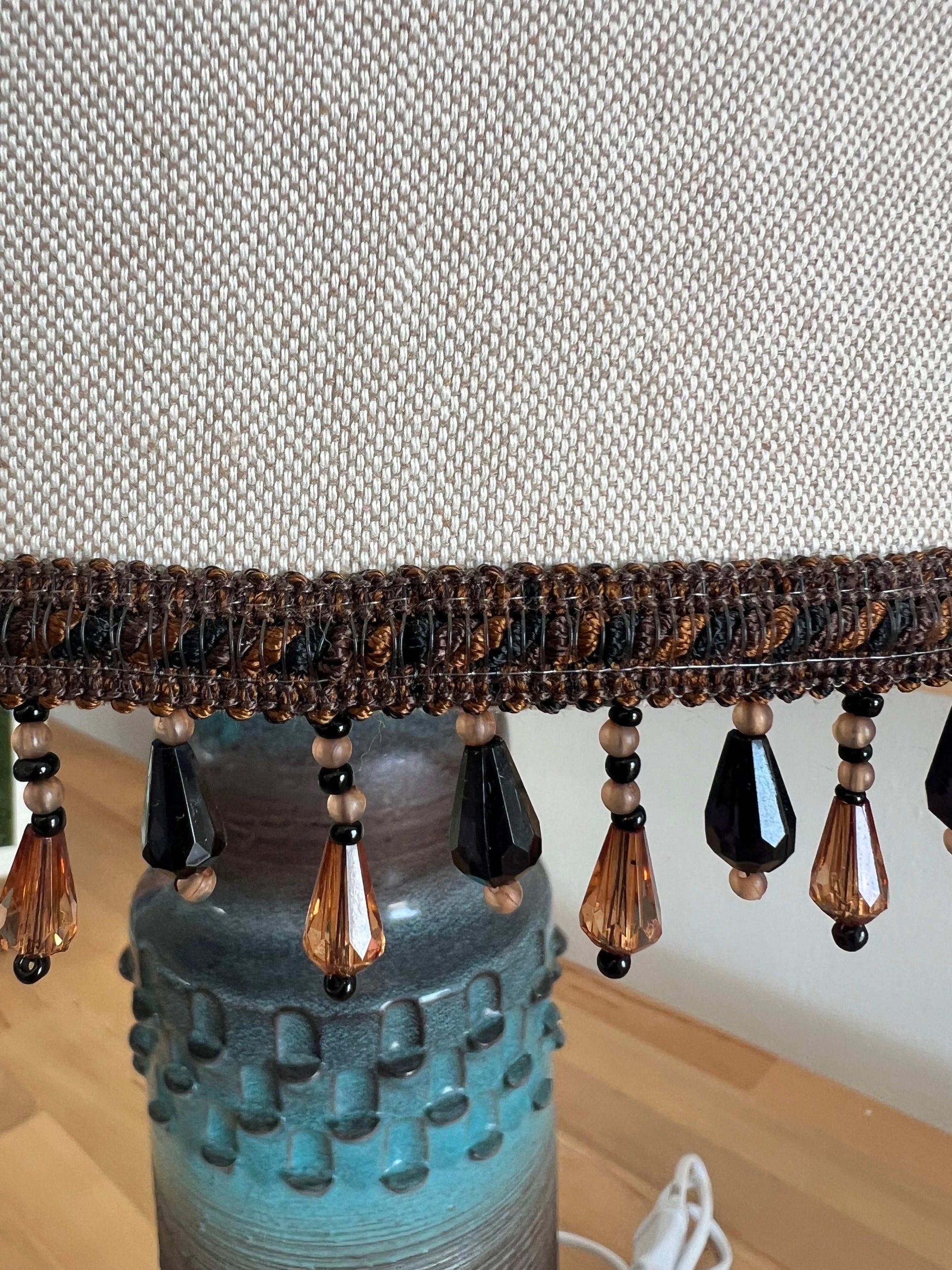 Decorative lamp with beaded shade against a textured wall.