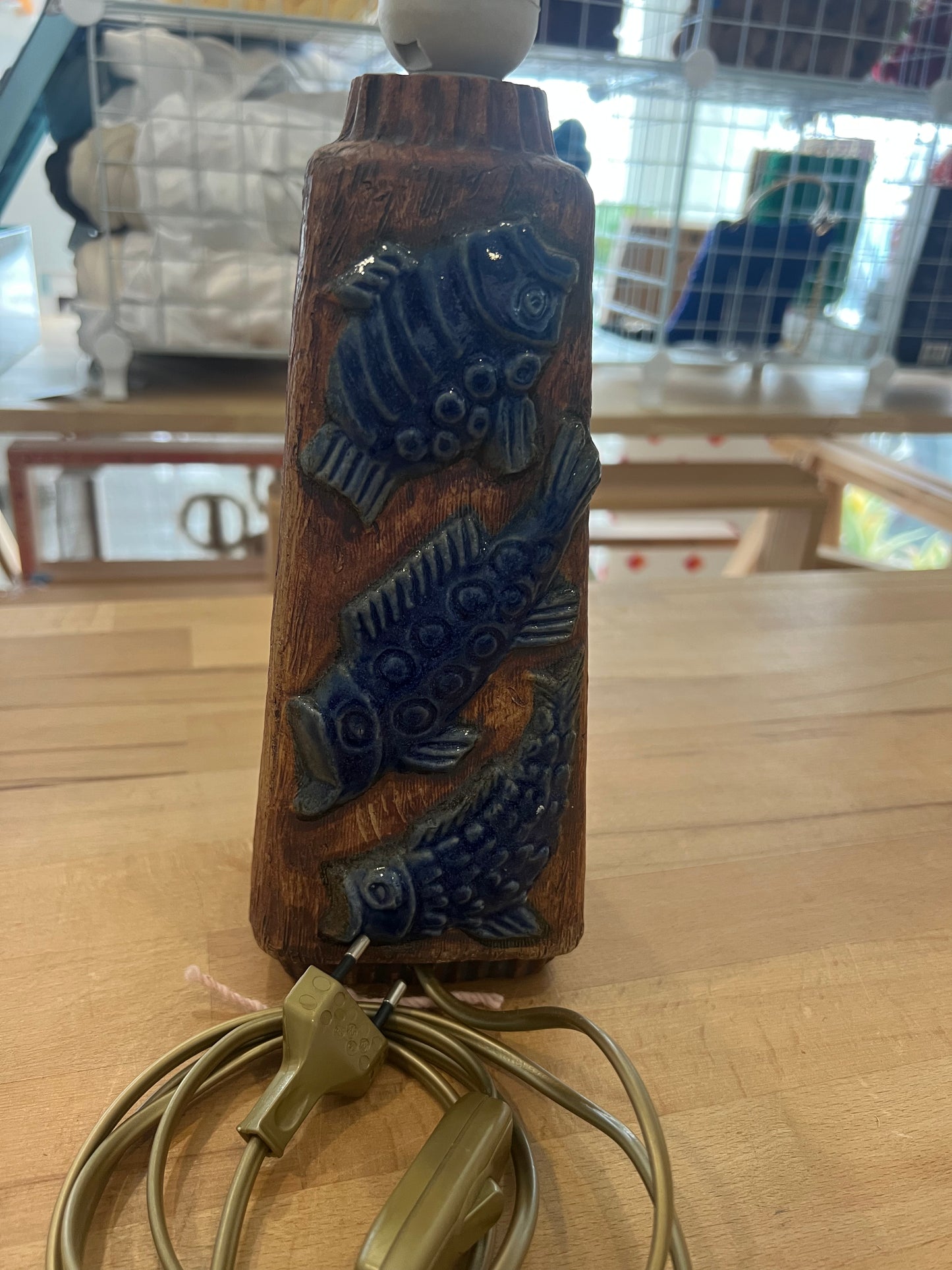Decorative ceramic lamp with blue fish design on a base, placed on a table.